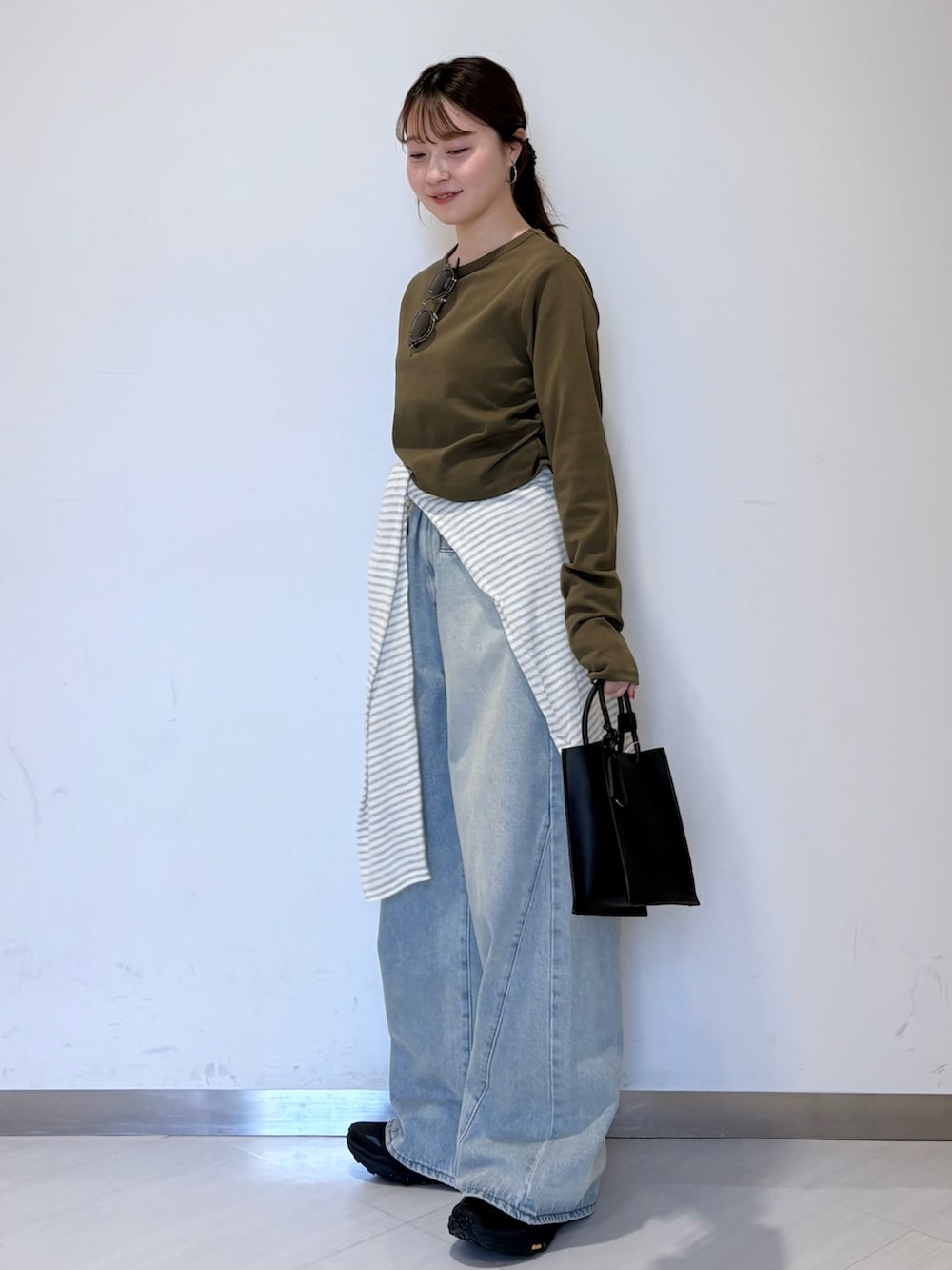 グリーン系のTシャツ/カットソー、ホワイト系のニット/セーター、ブラック系のハンドバッグを着用したレディースの春コーディネートの2枚目の写真