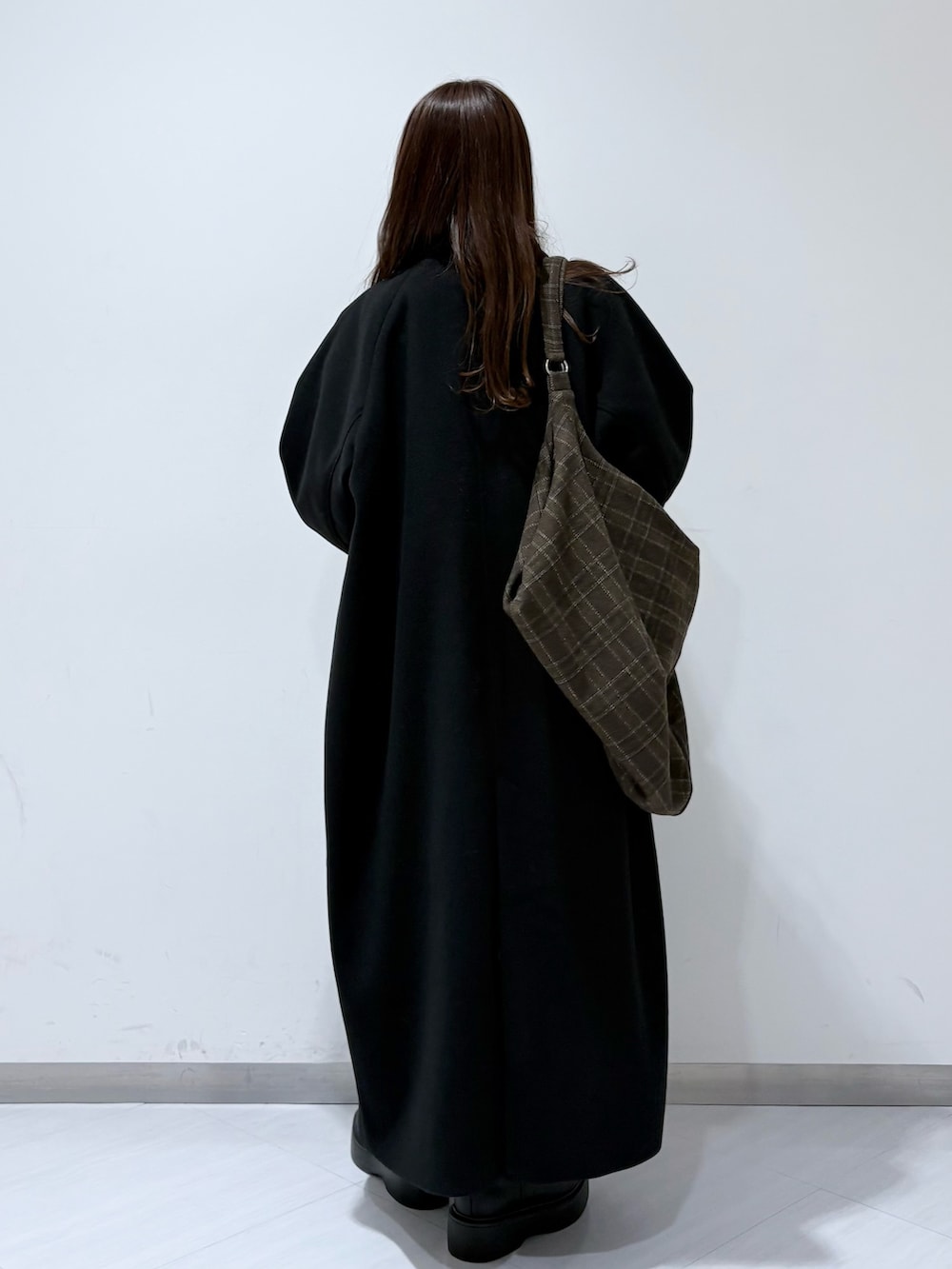 ブラック系のステンカラーコート、ブラウン系のワンピース、ブラック系のブーツを着用したレディースの秋コーディネートの3枚目の写真