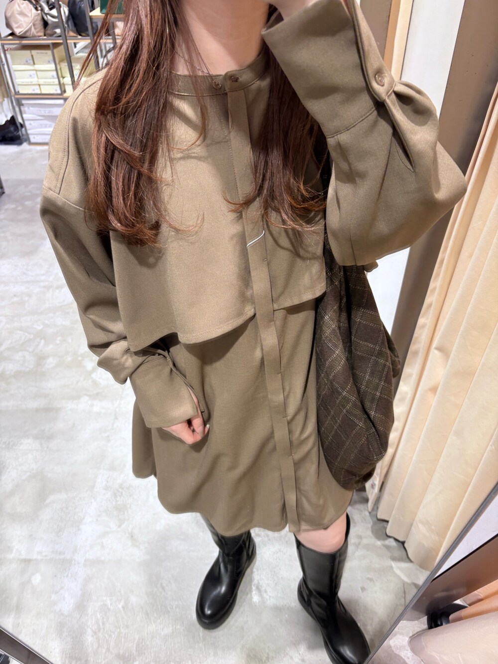 ブラック系のステンカラーコート、ブラウン系のワンピース、ブラック系のブーツを着用したレディースの秋コーディネートの6枚目の写真