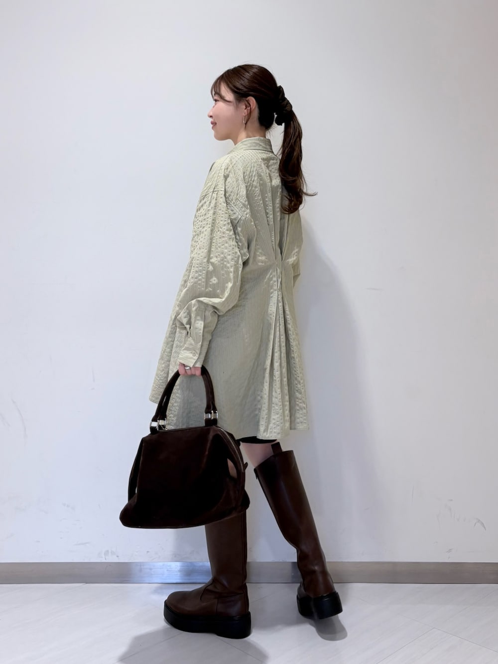 グリーン系のワンピース、ブラウン系のブーツ、ブラック系のその他パンツを着用したレディースの冬コーディネートの2枚目の写真