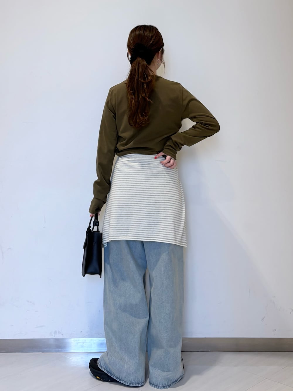 グリーン系のTシャツ/カットソー、ホワイト系のニット/セーター、ブラック系のハンドバッグを着用したレディースの春コーディネートの3枚目の写真