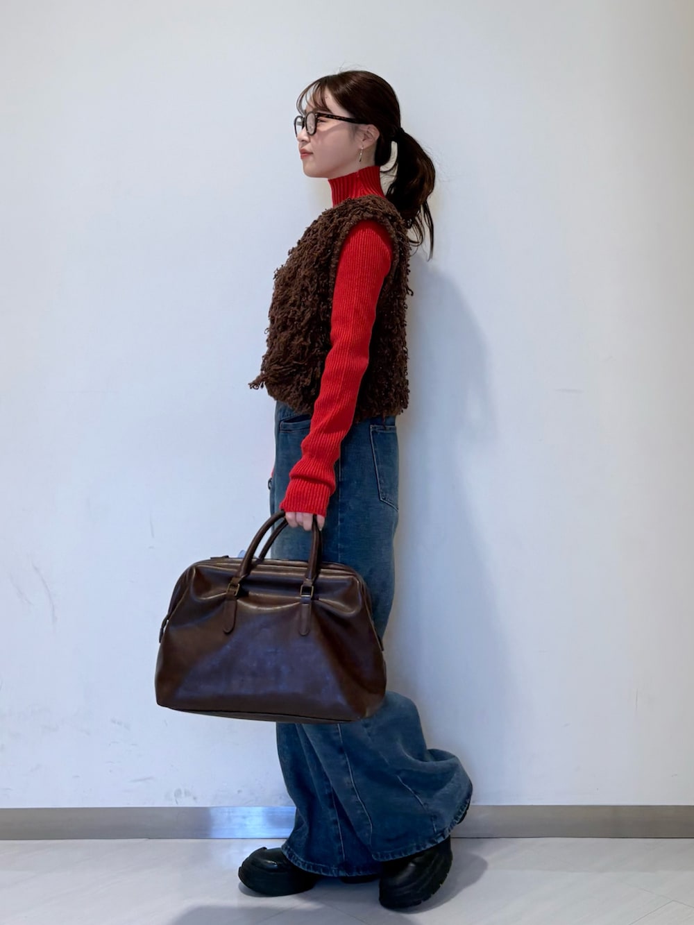 レッド系のニット/セーター、ブラウン系のベスト、ブルー系のデニムパンツを着用したレディースの冬コーディネートの2枚目の写真