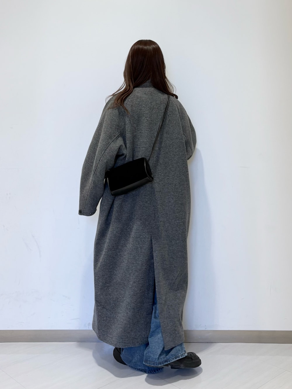 グレー系のステンカラーコート、ブラック系のショルダーバッグ、ブルー系のデニムパンツを着用したレディースの秋コーディネートの2枚目の写真