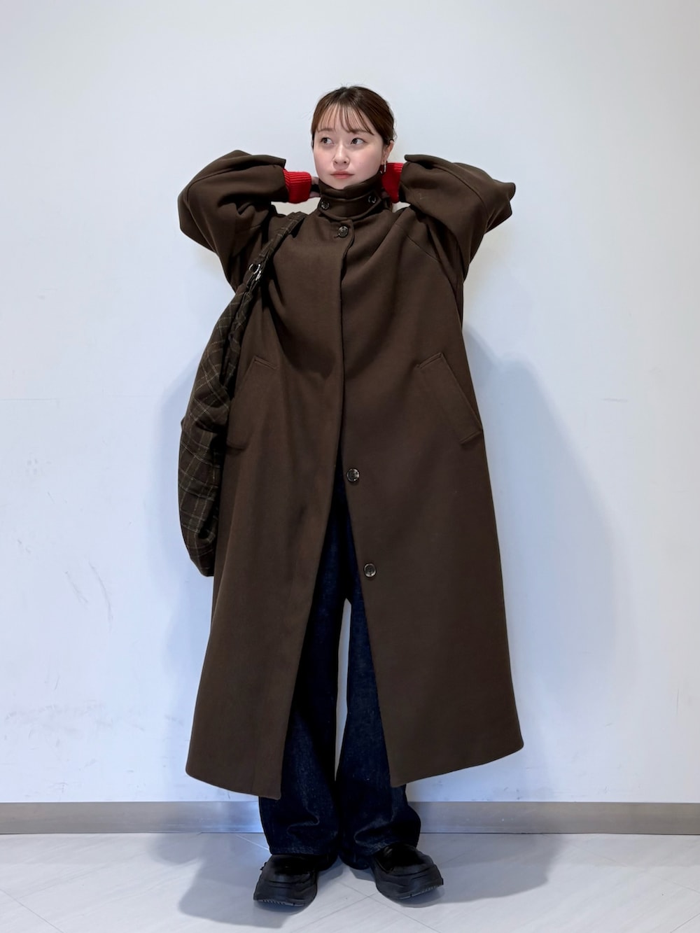 レッド系のニット/セーター、ブラウン系のステンカラーコート、ブルー系のデニムパンツを着用したレディースの冬コーディネートの2枚目の写真