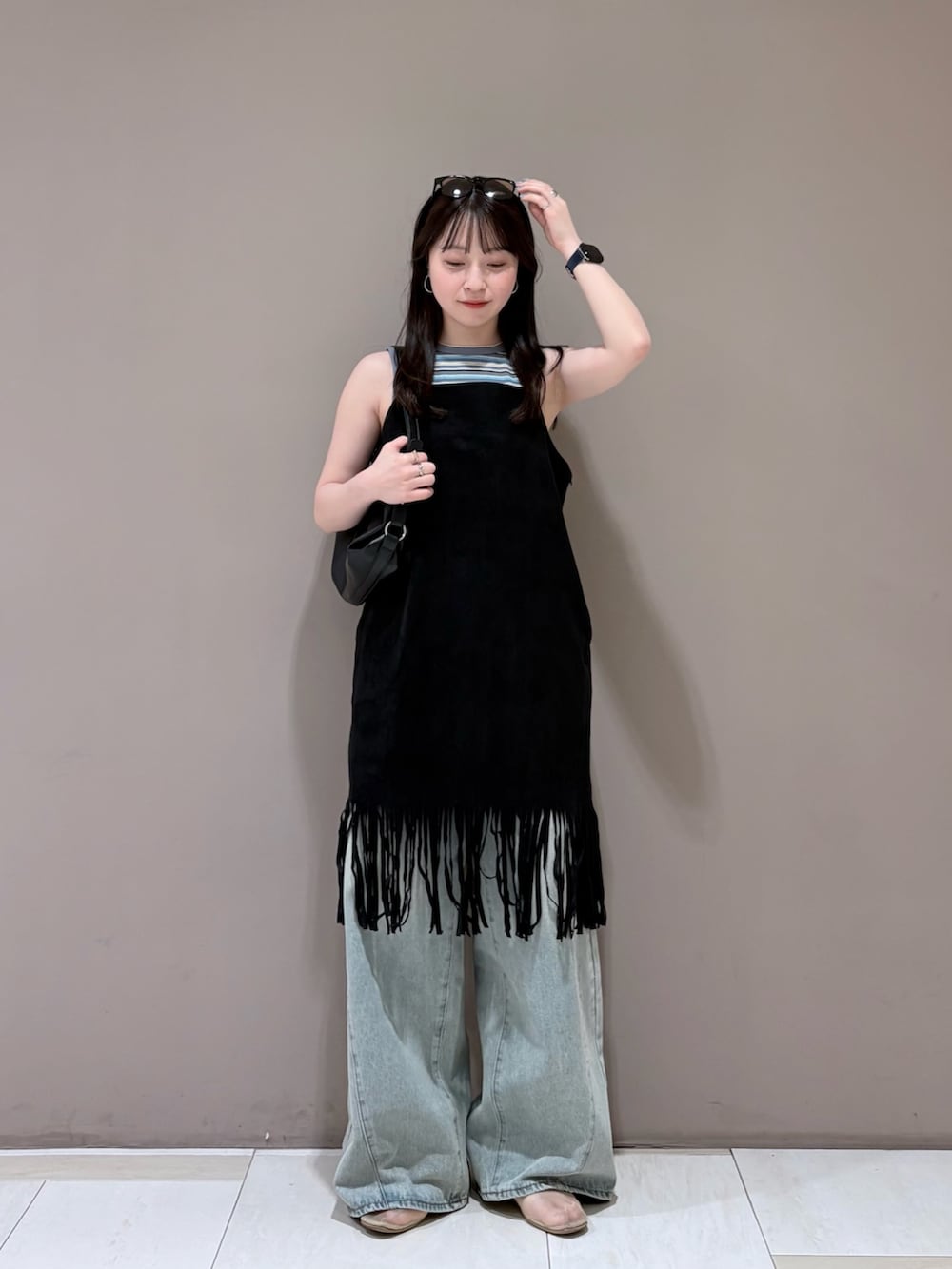 ブルー系のデニムパンツ、ブラック系のショルダーバッグ、ブルー系のタンクトップを着用したレディースの夏コーディネートの2枚目の写真