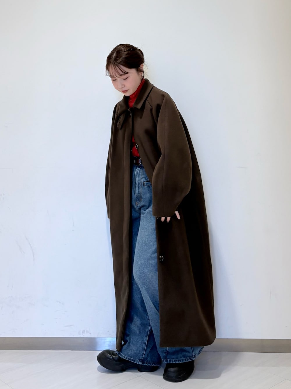 レッド系のニット/セーター、ブラウン系のステンカラーコート、ブルー系のデニムパンツを着用したレディースの秋コーディネートの2枚目の写真