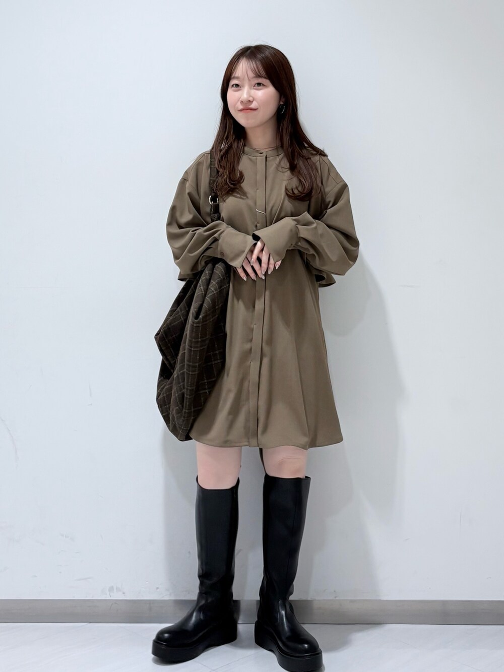 ブラック系のステンカラーコート、ブラウン系のワンピース、ブラック系のブーツを着用したレディースの秋コーディネートの5枚目の写真