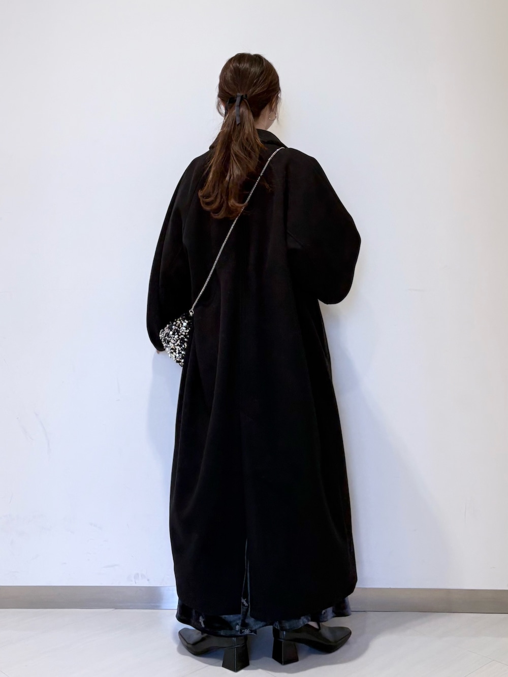 グレー系のワンピース、ブラック系のステンカラーコート、ブラック系のパンプスを着用したレディースの冬コーディネートの6枚目の写真