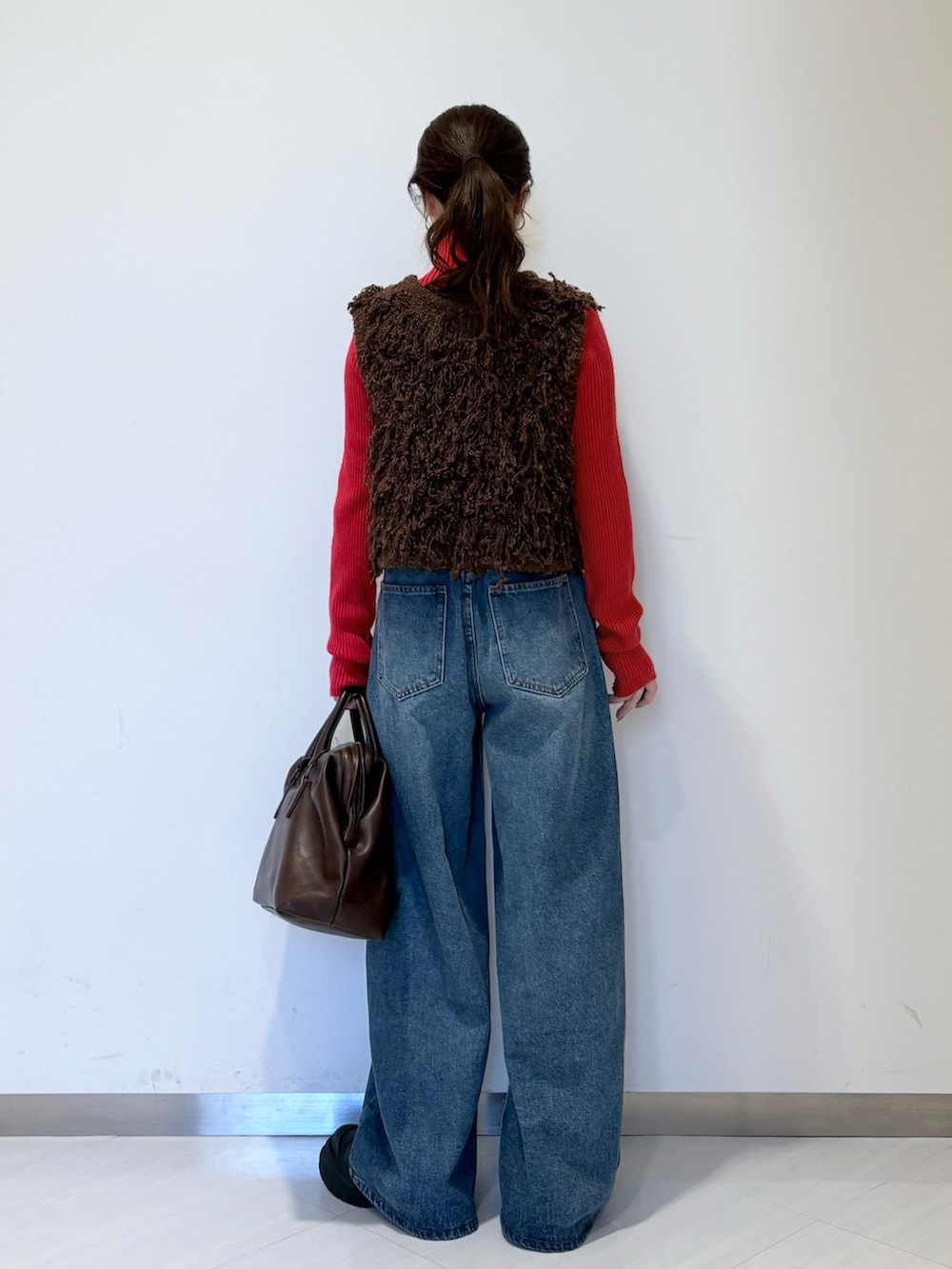 レッド系のニット/セーター、ブラウン系のベスト、ブルー系のデニムパンツを着用したレディースの冬コーディネートの3枚目の写真