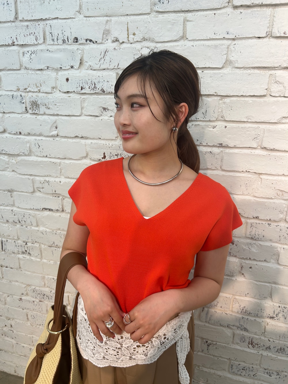 ベージュ系のその他パンツ、オレンジ系のニット/セーター、ベージュ系のハンドバッグを着用したレディースの夏コーディネートの3枚目の写真