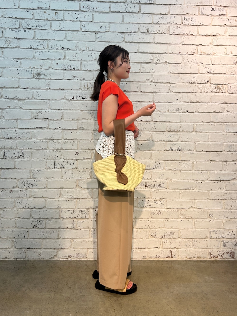 ベージュ系のその他パンツ、オレンジ系のニット/セーター、ベージュ系のハンドバッグを着用したレディースの夏コーディネートの5枚目の写真