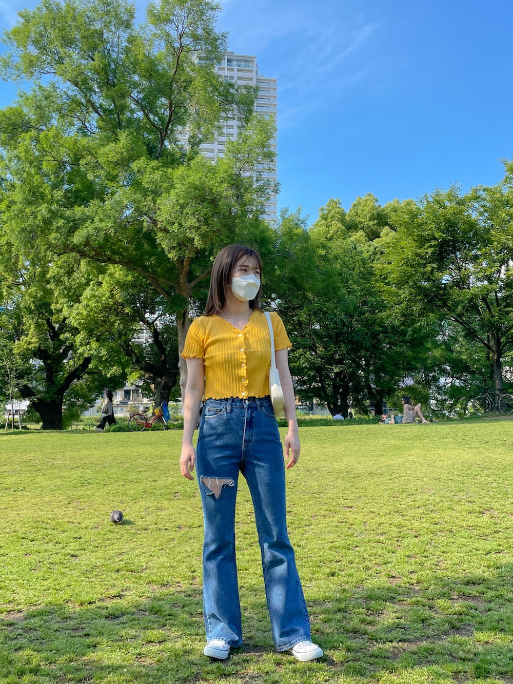 イエロー系のニット/セーター、ブルー系のデニムパンツ、ホワイト系のショルダーバッグを着用したレディースの夏コーディネートの2枚目の写真