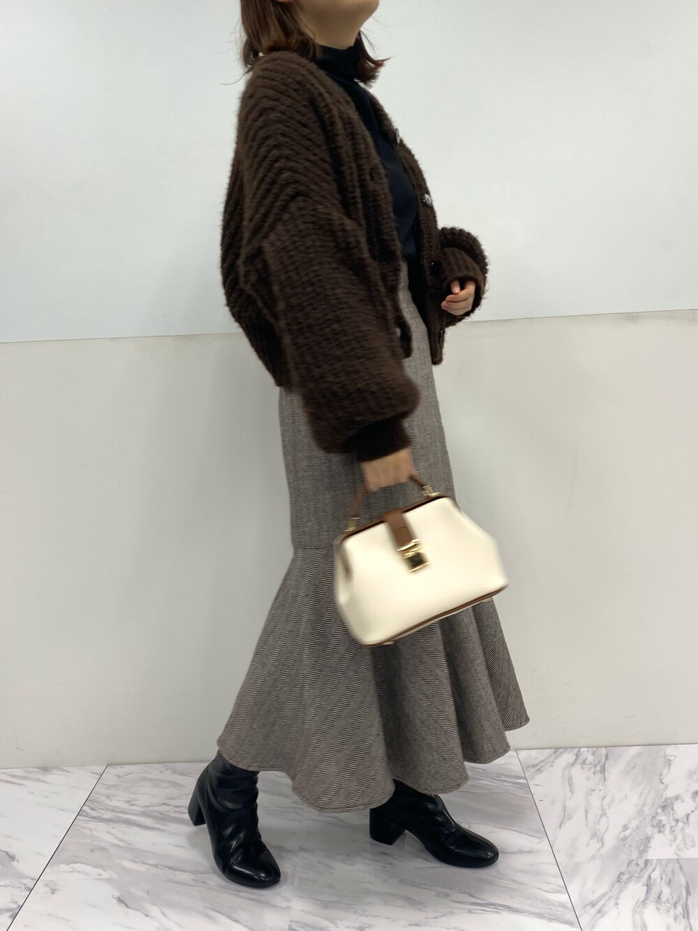 ホワイト系のショルダーバッグ、ブラウン系のカーディガン/ボレロ、ブラウン系のスカートを着用したレディースの秋コーディネートの3枚目の写真
