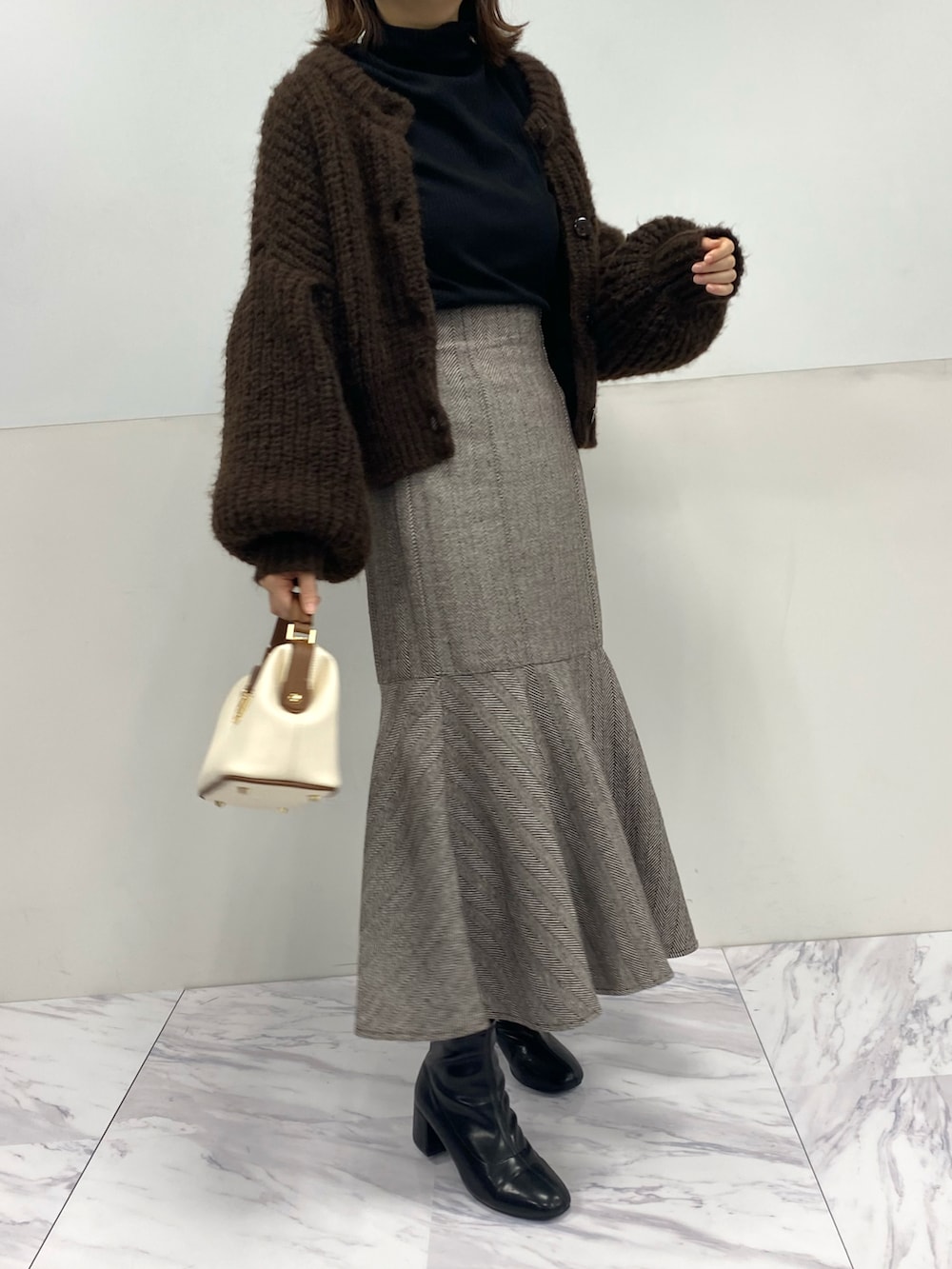 ホワイト系のショルダーバッグ、ブラウン系のカーディガン/ボレロ、ブラウン系のスカートを着用したレディースの秋コーディネートの2枚目の写真