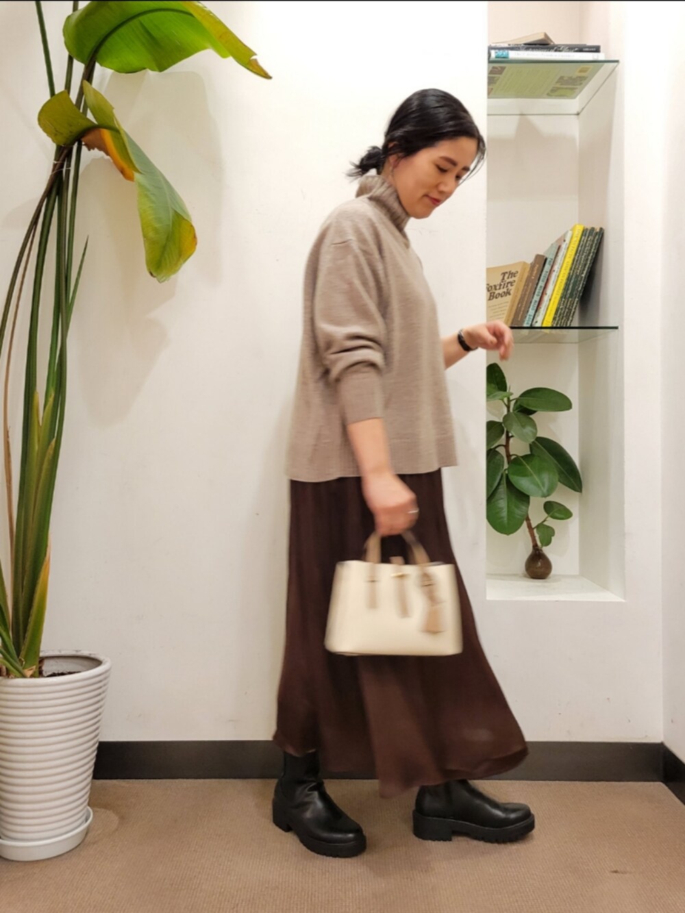 ブラック系のブーツ、ホワイト系のハンドバッグ、ブラウン系のスカートを着用したレディースの秋コーディネートの3枚目の写真