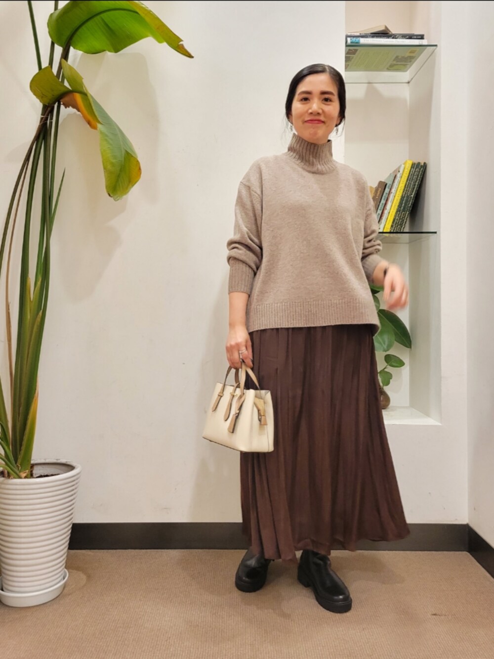 ブラック系のブーツ、ホワイト系のハンドバッグ、ブラウン系のスカートを着用したレディースの秋コーディネートの2枚目の写真