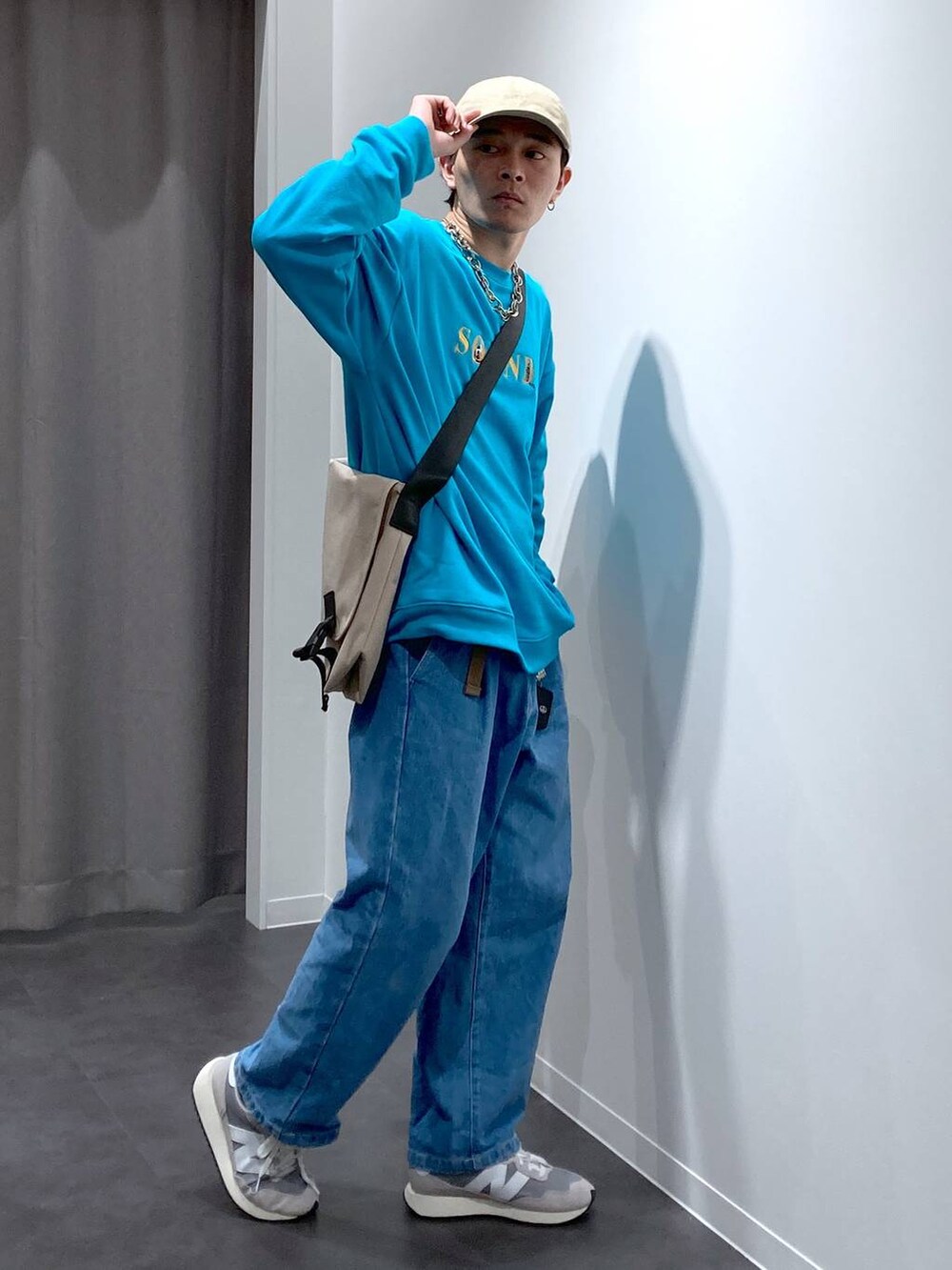 グレー系のスニーカー、ベージュ系のメッセンジャーバッグ、ブルー系のデニムパンツを着用したメンズの冬コーディネートの3枚目の写真