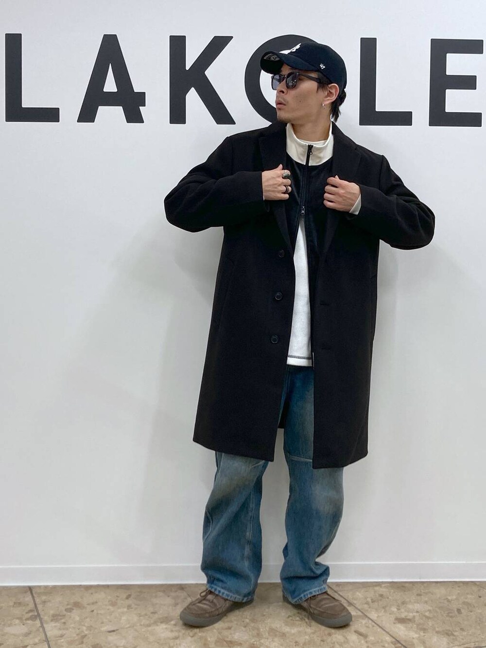 ブラック系のチェスターコート、ブルー系のデニムパンツ、ホワイト系のTシャツ/カットソーを着用したメンズの秋コーディネートの4枚目の写真