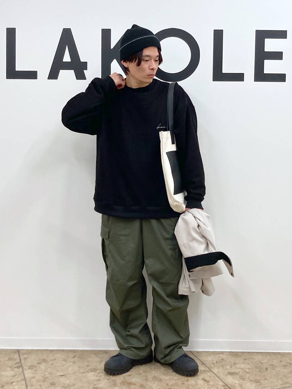 ベージュ系のトートバッグ、ブラック系のその他トップス、グリーン系のカーゴパンツを着用したメンズの冬コーディネートの5枚目の写真