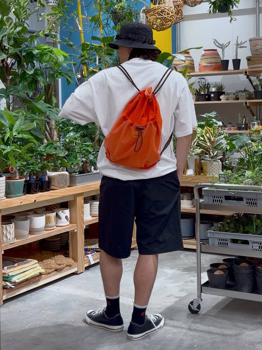 ブラック系のスニーカー、オレンジ系のバックパック/リュック、ホワイト系のTシャツ/カットソーを着用したメンズの春コーディネートの2枚目の写真