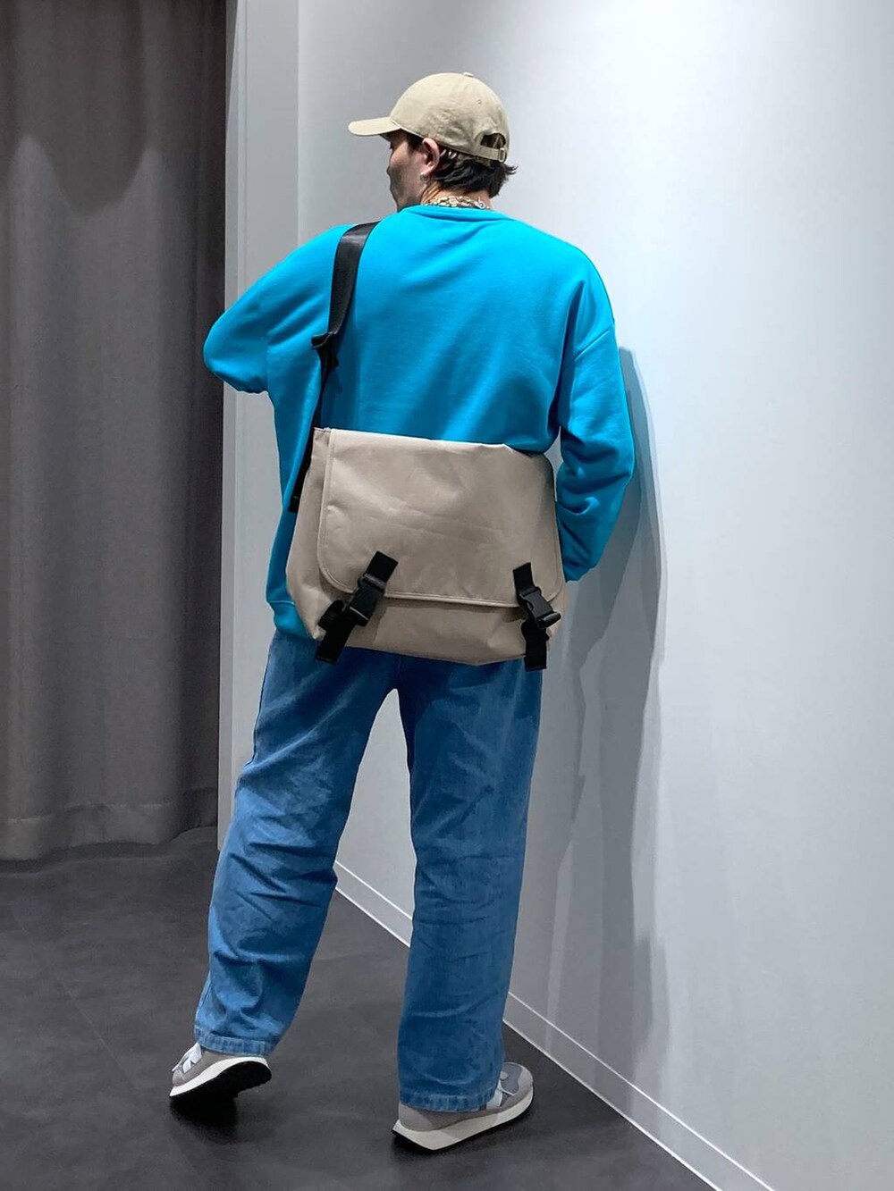 グレー系のスニーカー、ベージュ系のメッセンジャーバッグ、ブルー系のデニムパンツを着用したメンズの冬コーディネートの2枚目の写真