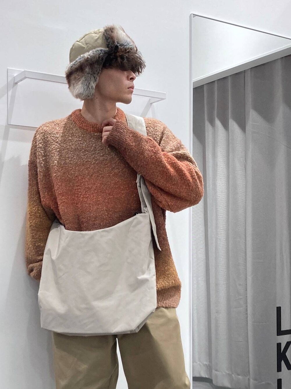 ホワイト系のスニーカー、オレンジ系のニット/セーター、ベージュ系のチノパンツを着用したメンズの秋コーディネートの5枚目の写真