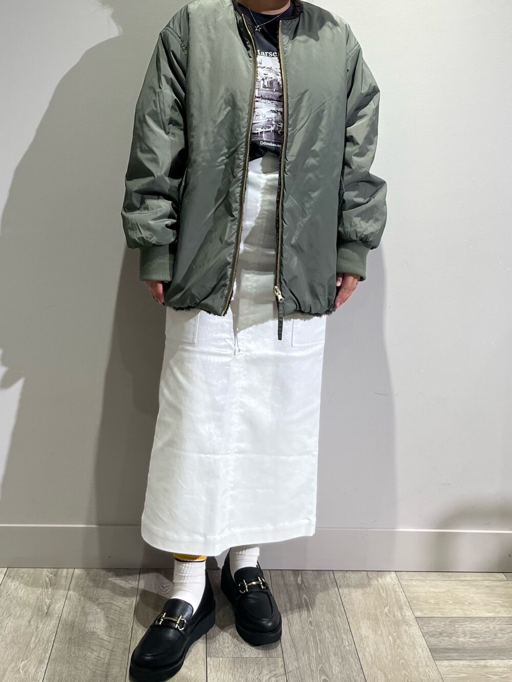 グリーン系のブルゾン、グレー系のTシャツ/カットソー、シルバー系のスカートを着用したレディースの秋コーディネートの5枚目の写真