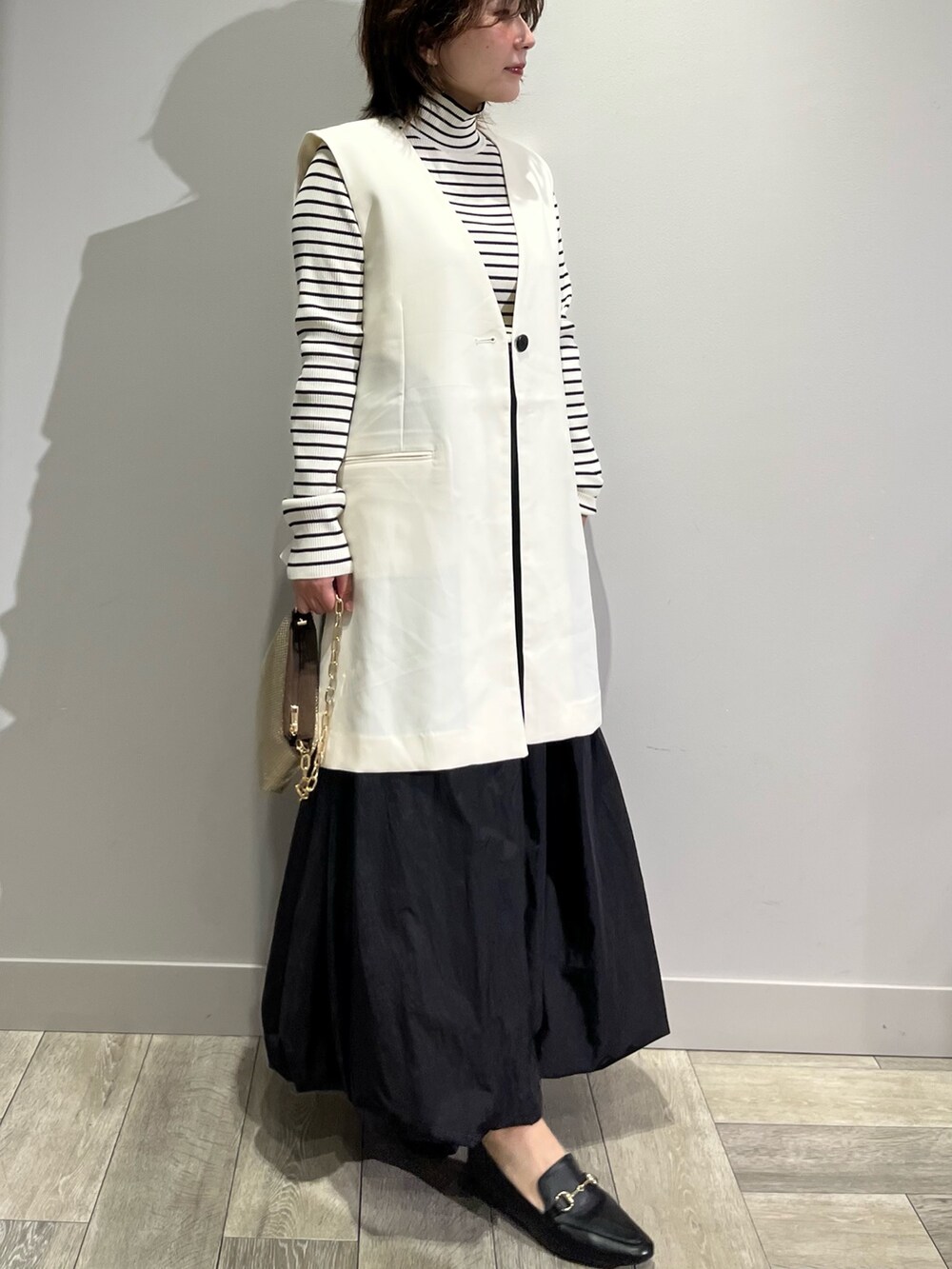 ホワイト系のベスト、ブラック系のスカートを着用したレディースの秋コーディネートの2枚目の写真