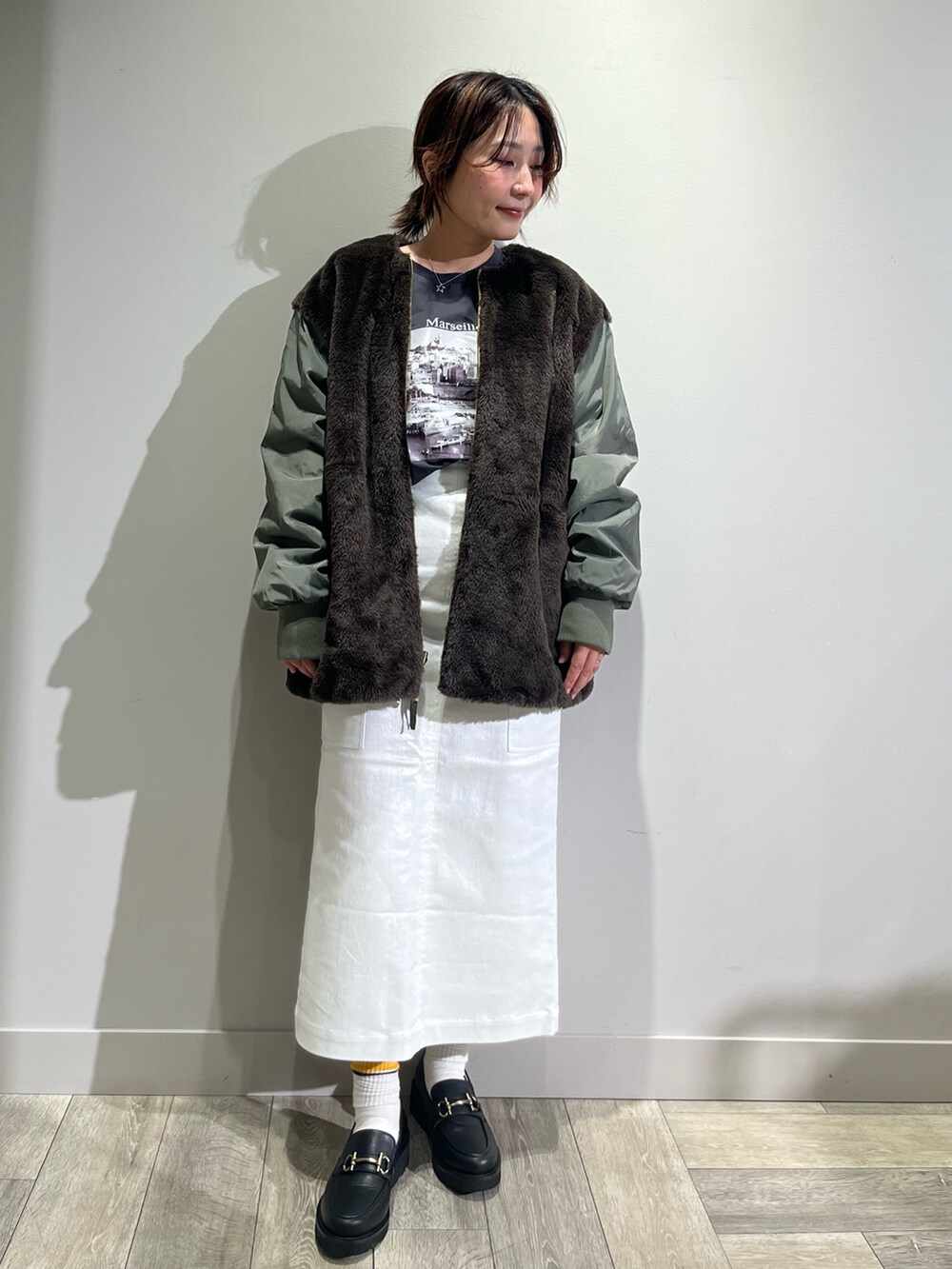グリーン系のブルゾン、グレー系のTシャツ/カットソー、シルバー系のスカートを着用したレディースの秋コーディネートの2枚目の写真