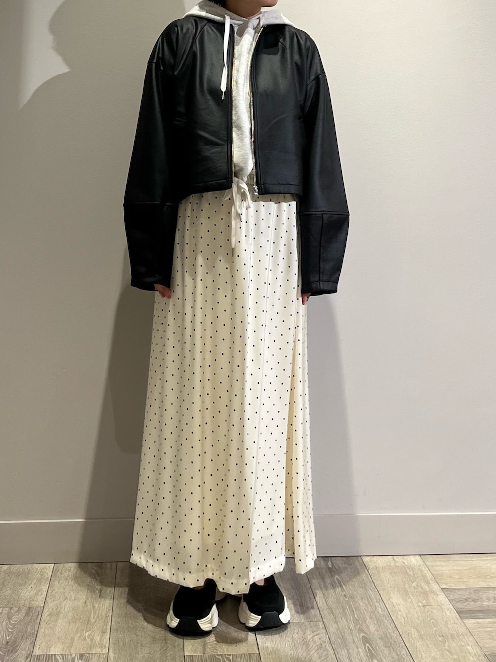 ブラック系のブルゾン、グレー系のパーカー、ホワイト系のスカートを着用したレディースの春コーディネートの2枚目の写真