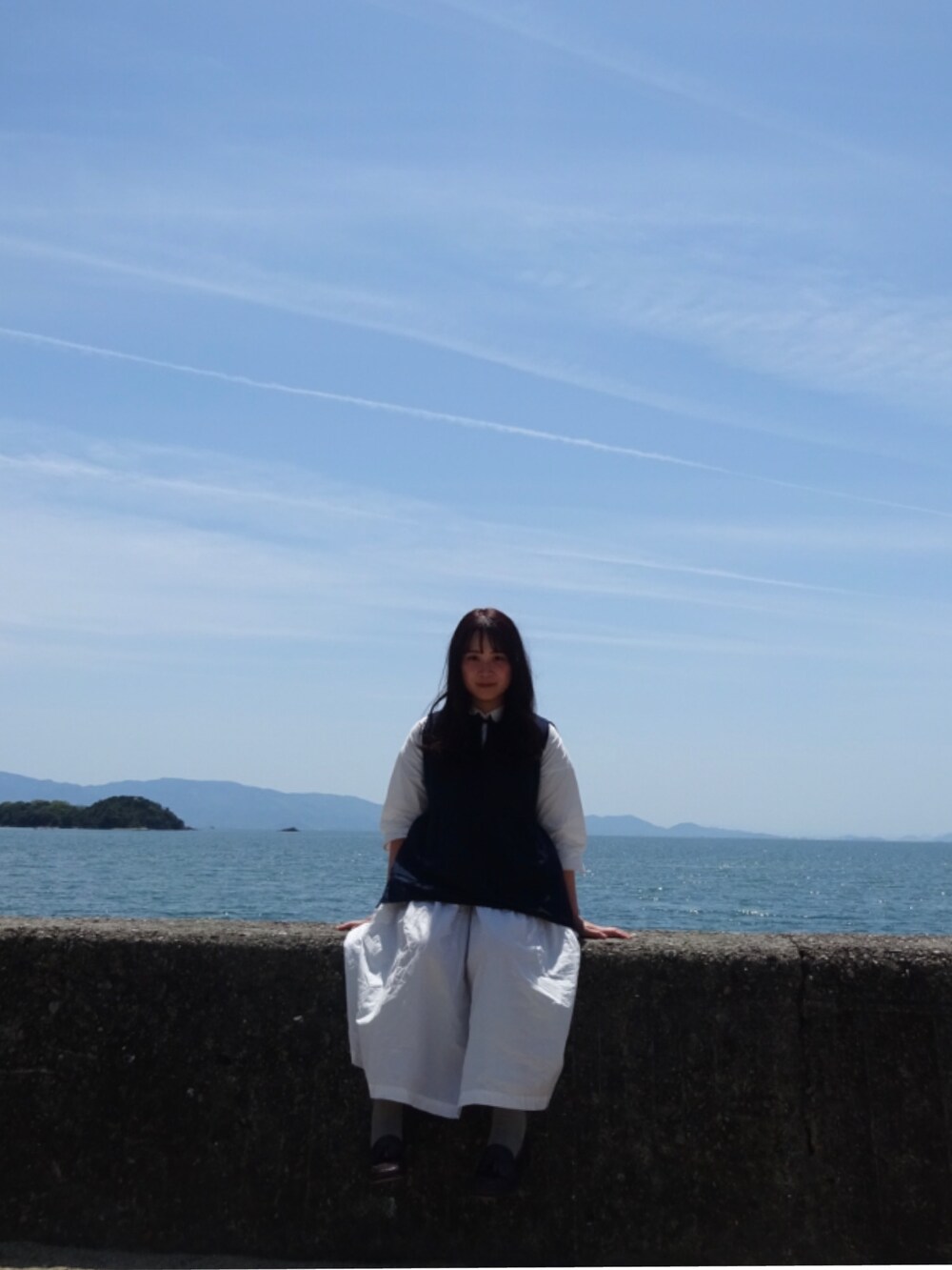 ホワイト系のシャツワンピース、ブルー系のトップス、ブラウン系のローファーを着用したレディースの夏コーディネートの2枚目の写真