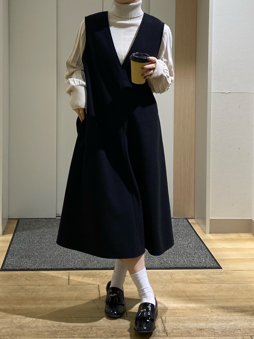 ホワイト系のニット/セーター、ベージュ系のニット/セーター、ブラック系のジャンパースカートを着用したレディースの秋コーディネートの2枚目の写真