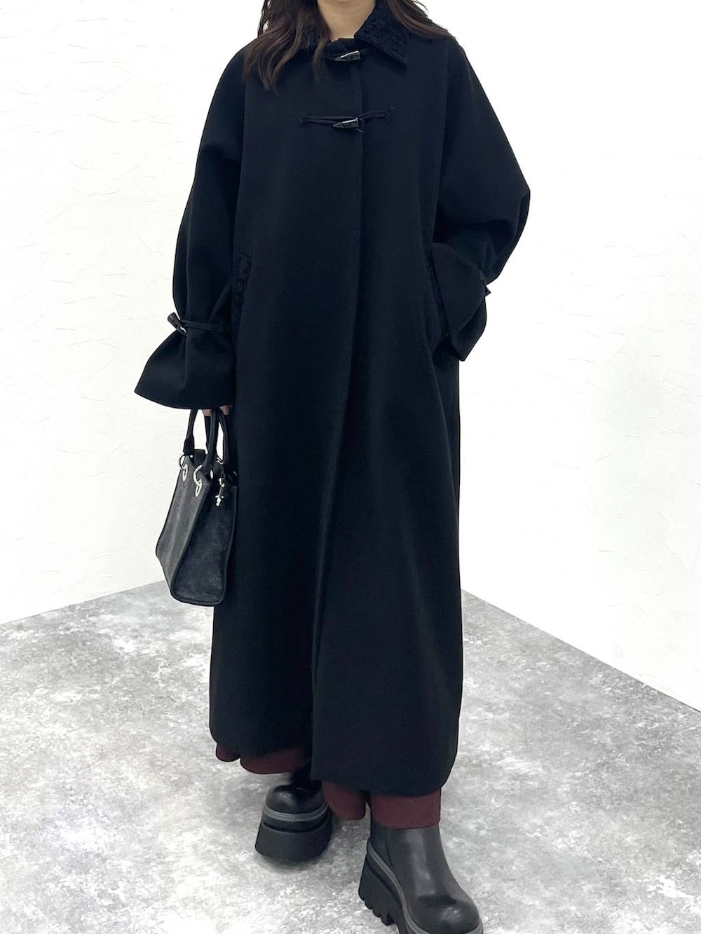 ブラック系のステンカラーコート、ブラック系のショルダーバッグ、レッド系のワンピースを着用したレディースの冬コーディネートの5枚目の写真