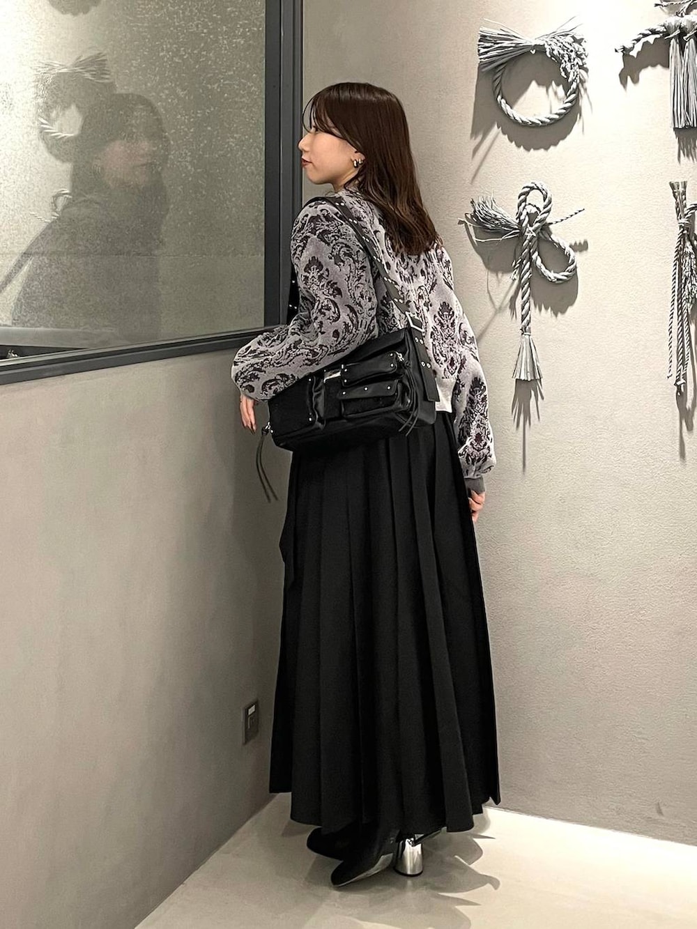 グレー系のニット/セーター、ブラック系のブーツ、ブラック系のショルダーバッグを着用したレディースの秋コーディネートの2枚目の写真