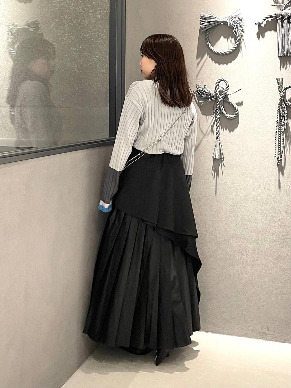 ブラック系のスカート、ブラック系のパンプス、グレー系のニット/セーターを着用したレディースの秋コーディネートの2枚目の写真