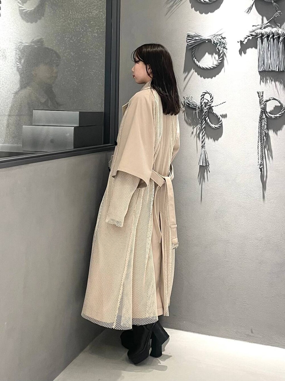 イエロー系のスカート、ブラック系のブーツ、ホワイト系のトレンチコートを着用したレディースの冬コーディネートの3枚目の写真