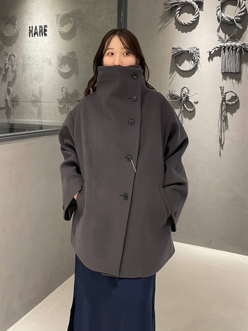 グレー系のチェスターコート、ブラック系のブーツ、ブルー系のワンピースを着用したレディースの秋コーディネートの4枚目の写真