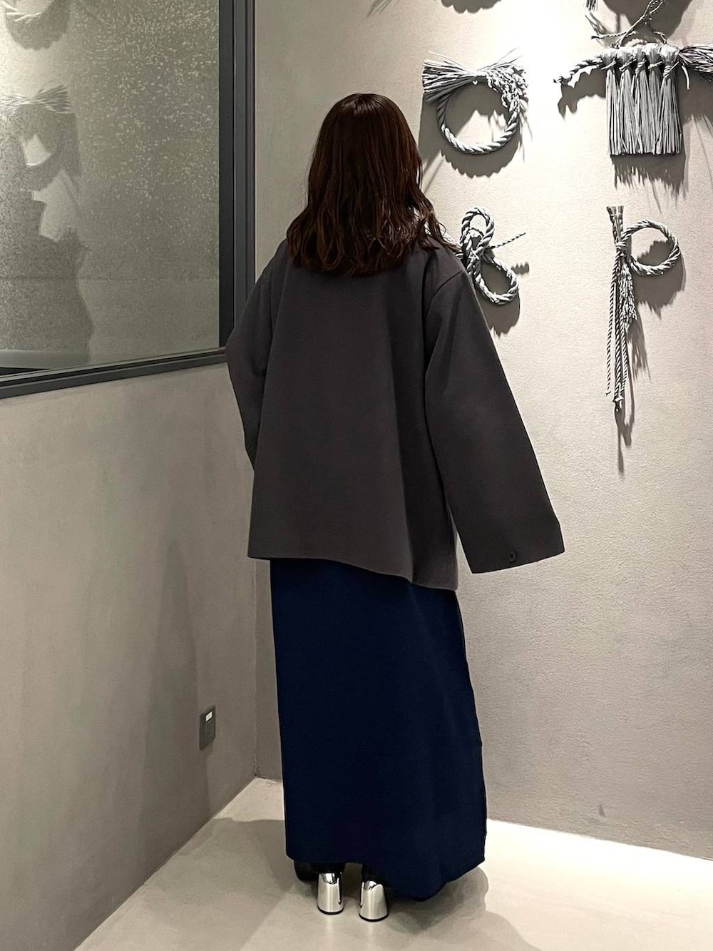 グレー系のチェスターコート、ブラック系のブーツ、ブルー系のワンピースを着用したレディースの秋コーディネートの3枚目の写真