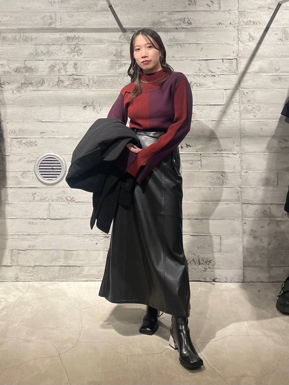 ブラック系のトレンチコート、ブラック系のブーツ、レッド系のニット/セーターを着用したレディースの秋コーディネートの2枚目の写真