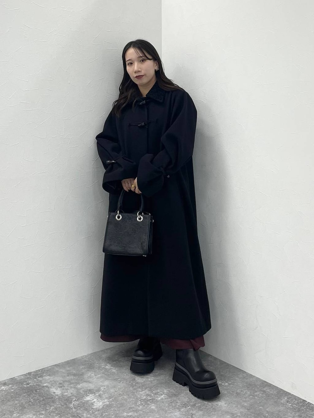 ブラック系のステンカラーコート、ブラック系のショルダーバッグ、レッド系のワンピースを着用したレディースの冬コーディネートの2枚目の写真