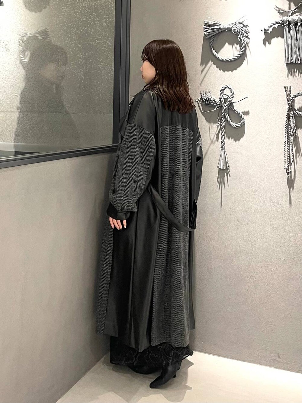 グレー系のチェスターコート、ブラック系のブーツ、ブルー系のニット/セーターを着用したレディースの秋コーディネートの2枚目の写真