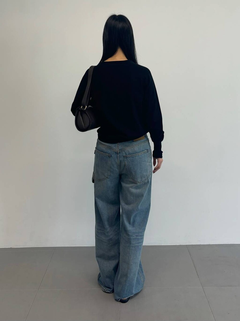 ブルー系のデニムパンツ、ブラック系のニット/セーター、ブラック系のベルトを着用したレディースの冬コーディネートの3枚目の写真