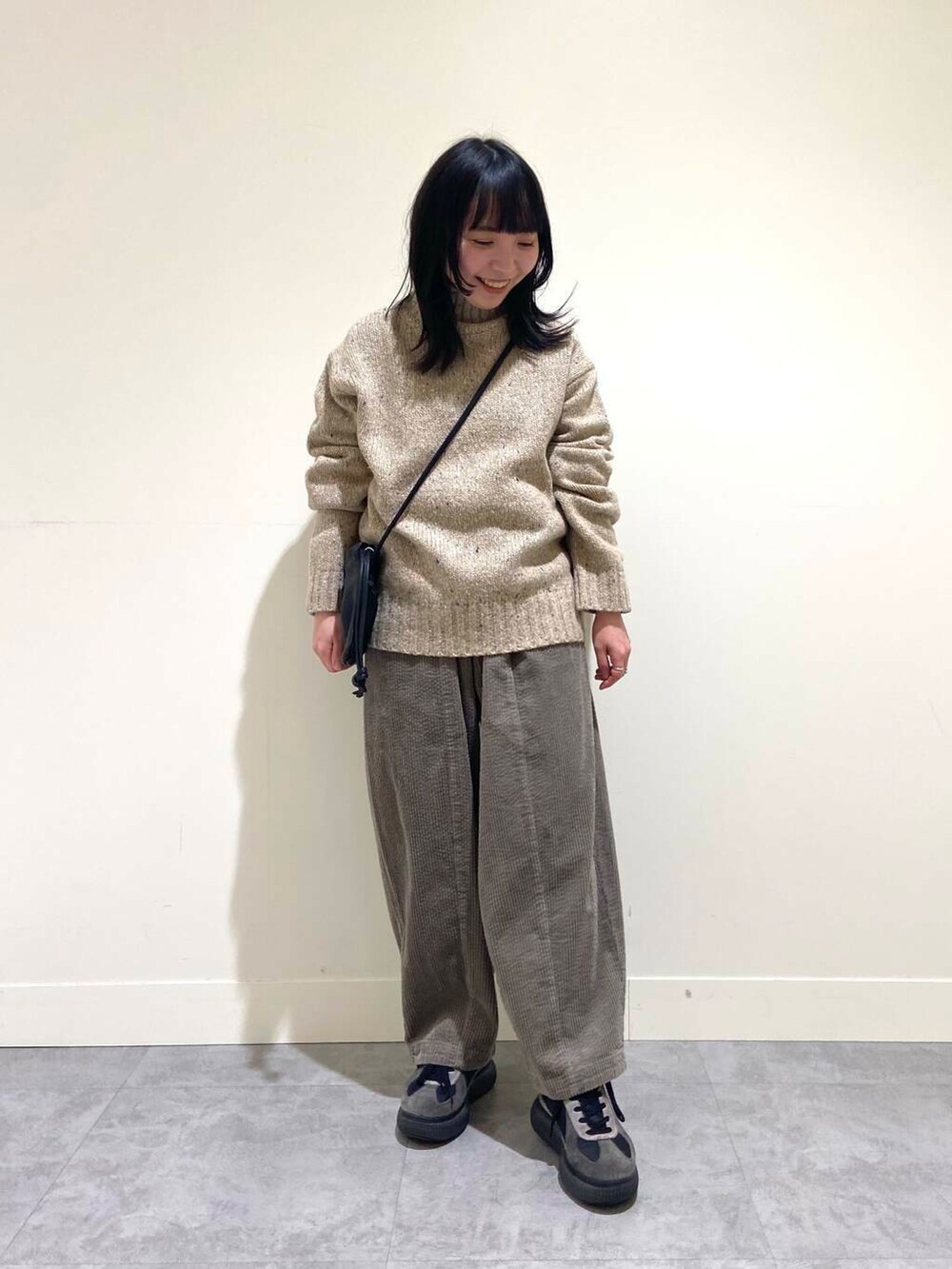 ベージュ系のニット/セーター、グレー系のその他パンツ、ブラック系のショルダーバッグを着用したレディースの冬コーディネートの2枚目の写真