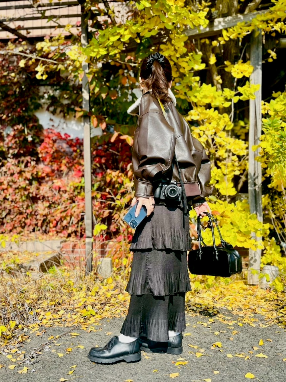 ブラウン系のブルゾン、ブラック系のスカート、ブラック系のボストンバッグを着用したレディースの秋コーディネートの2枚目の写真