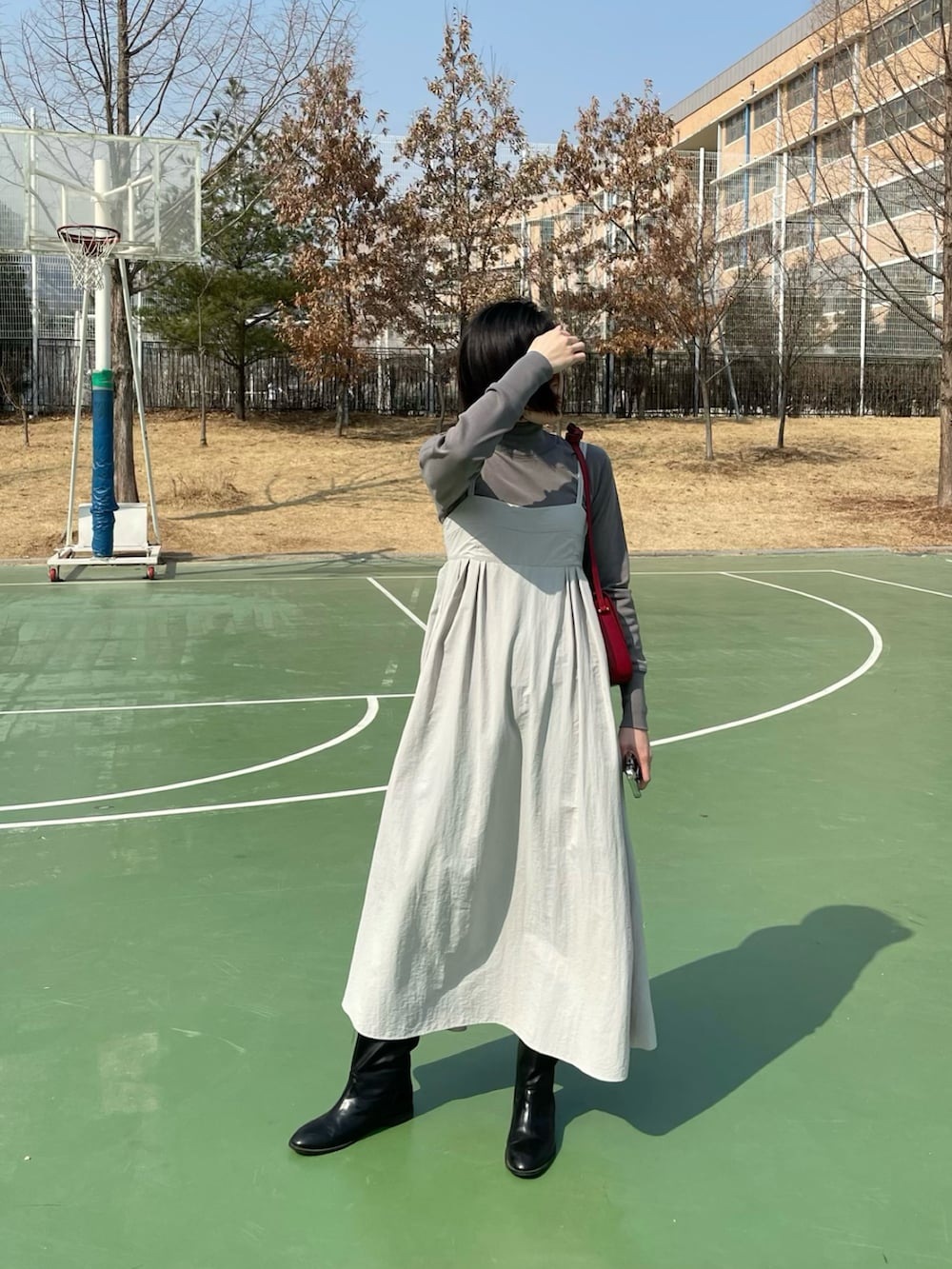 グレー系のワンピース、レッド系のショルダーバッグ、ブラック系のブーツを着用したレディースの春コーディネートの2枚目の写真