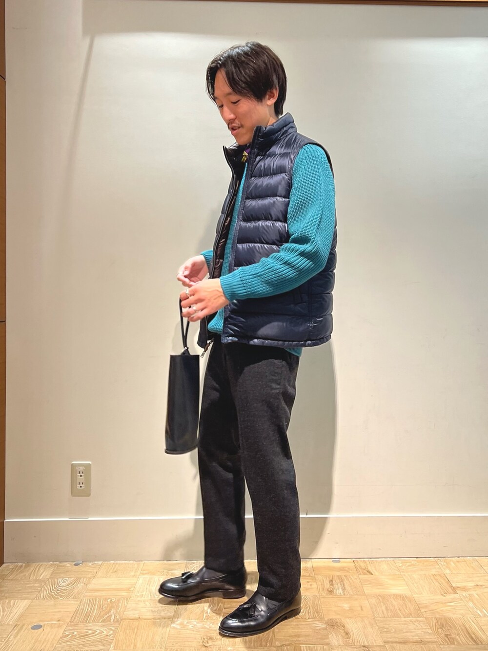 ブラウン系のダウンベスト、ブラック系のハンドバッグを着用したメンズの春コーディネートの4枚目の写真