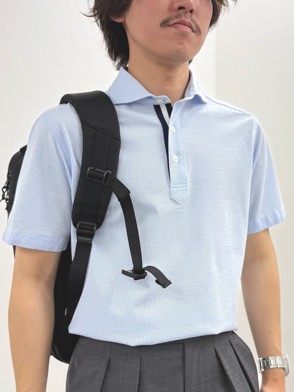 ブルー系のポロシャツ、グレー系のスラックス、ブラック系のバックパック/リュックを着用したメンズの春コーディネートの8枚目の写真