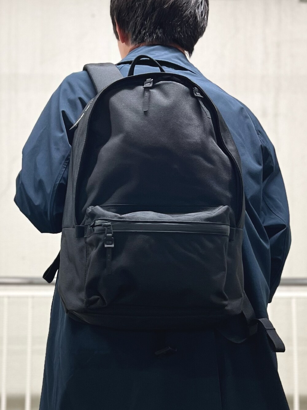 ブラック系のバックパック/リュック、ホワイト系のTシャツ/カットソー、ブルー系のステンカラーコートを着用したメンズの秋コーディネートの9枚目の写真