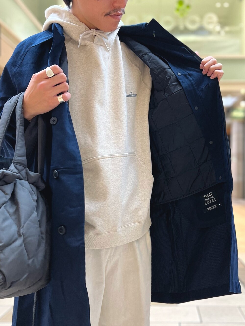 グレー系のパーカー、ブルー系のステンカラーコート、グレー系のトートバッグを着用したメンズの冬コーディネートの6枚目の写真