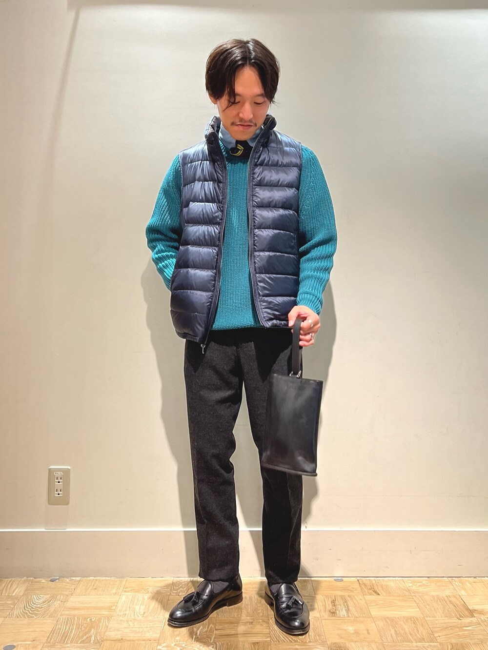 ブラウン系のダウンベスト、ブラック系のハンドバッグを着用したメンズの春コーディネートの2枚目の写真